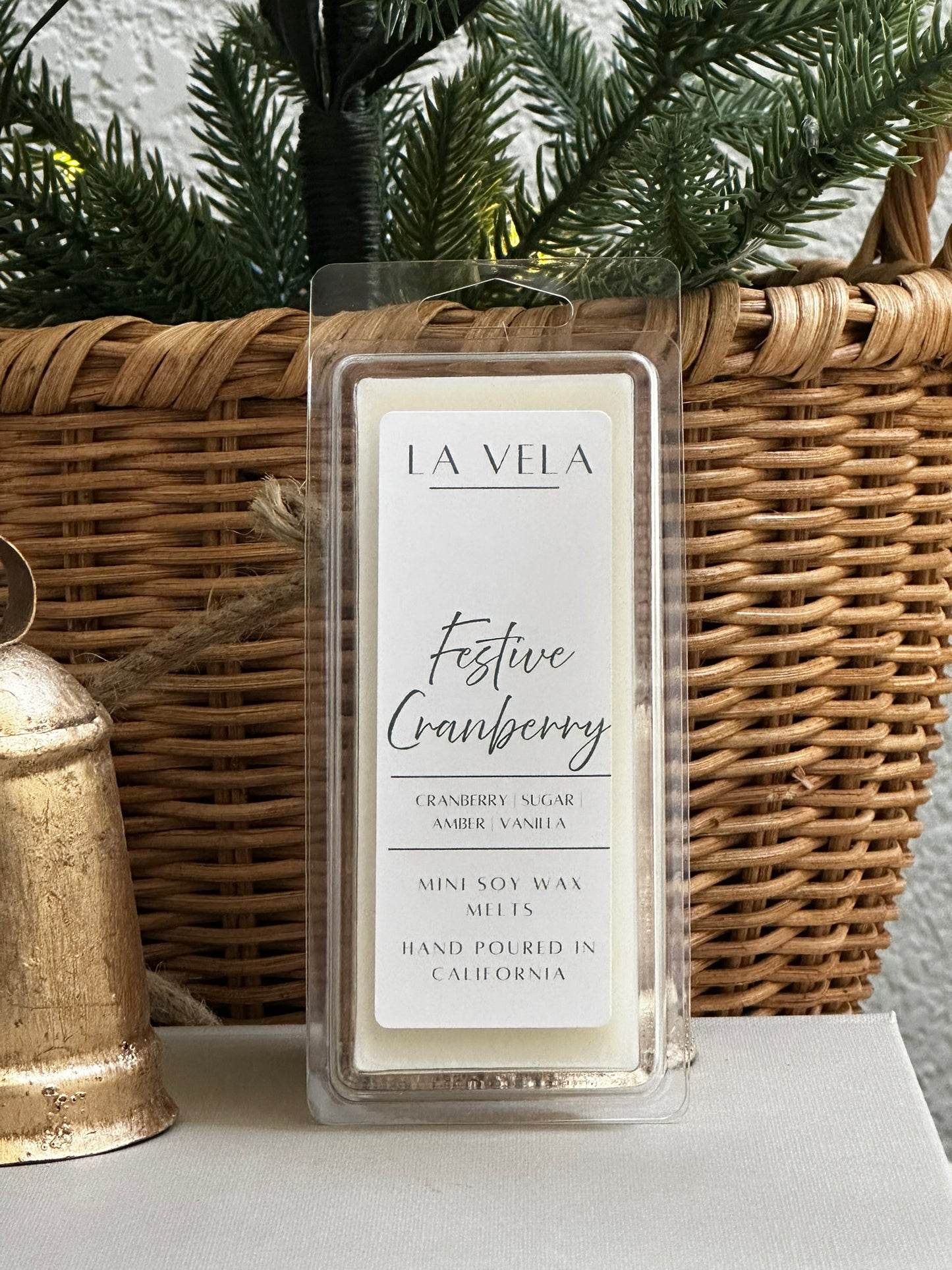 La Vela Festive Cranberry wax melt in front of a wicker basket and Christmas tree.