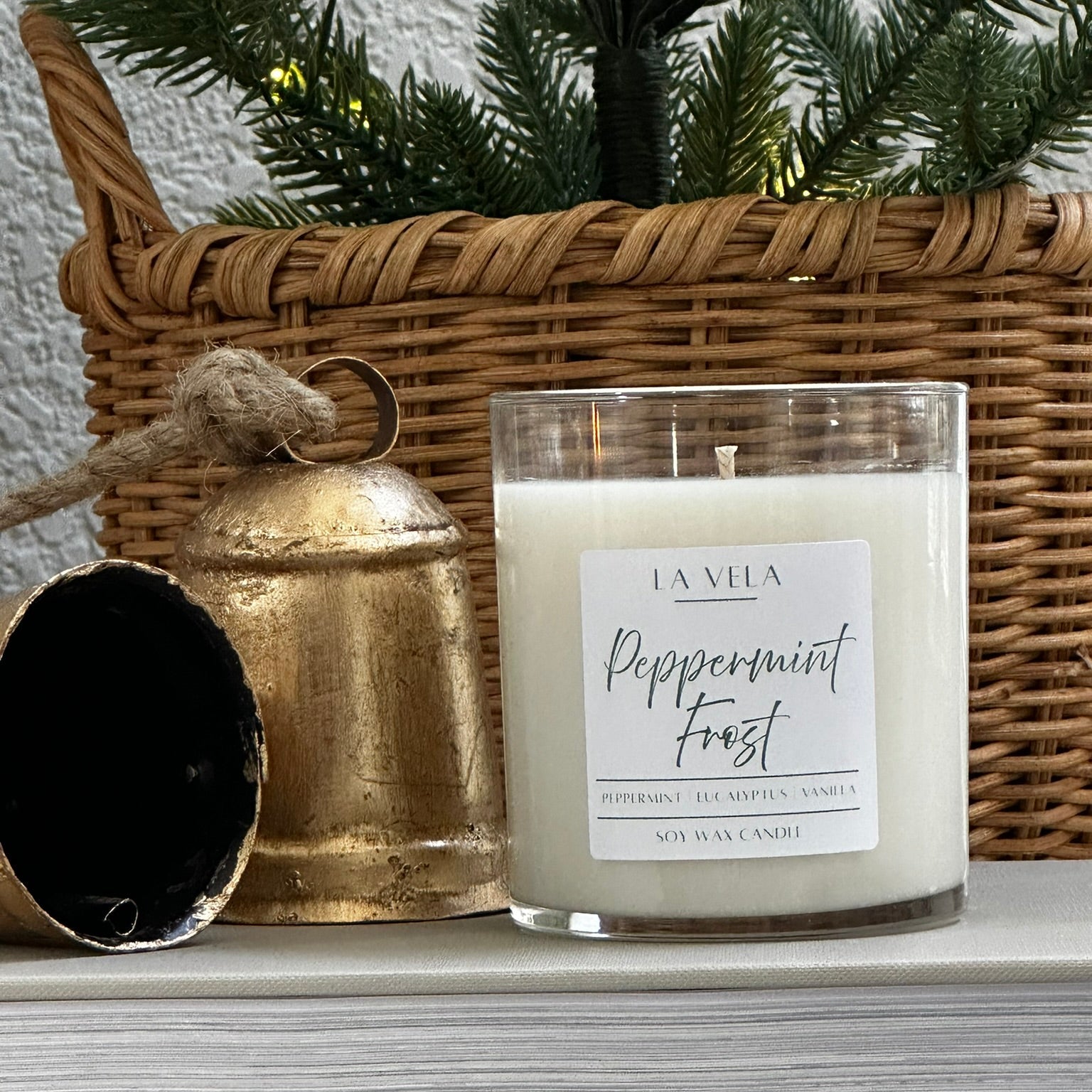 Candle labeled 'Peppermint Frost' with a wicker basket and gold bell in the background.