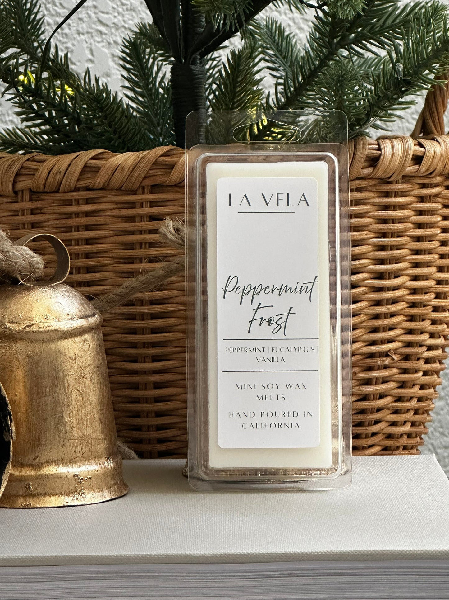 La Vela peppermint frost wax melt packaging with a wicker basket and gold bell in the background.