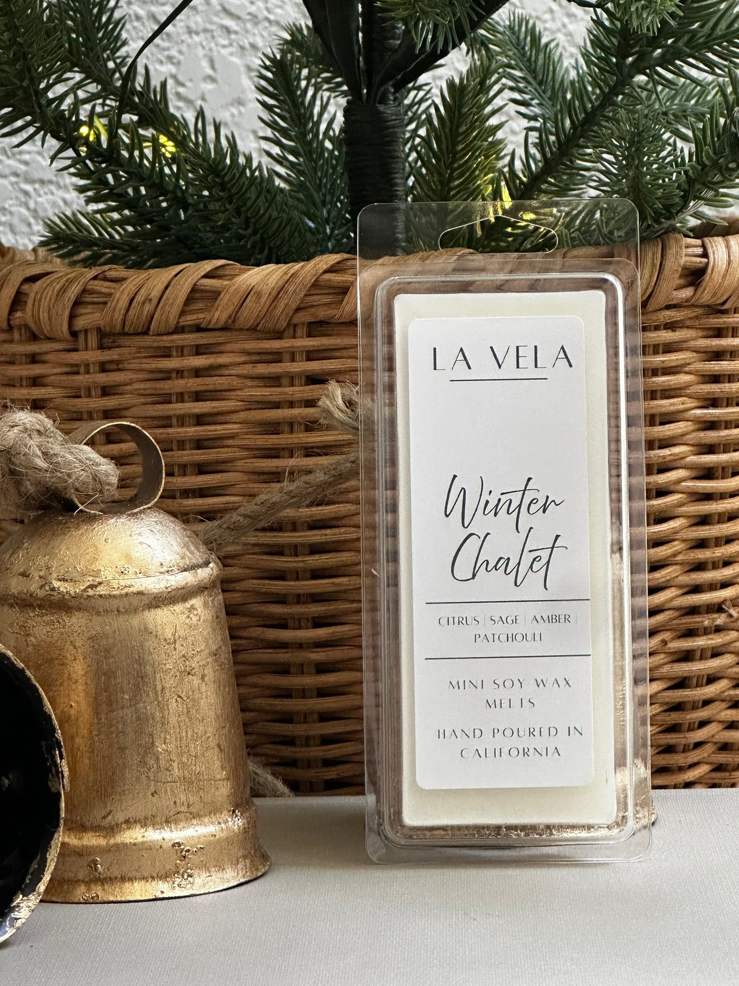 La Vela Winter Chalet wax melt with decorative elements like a wicker basket and gold bell.